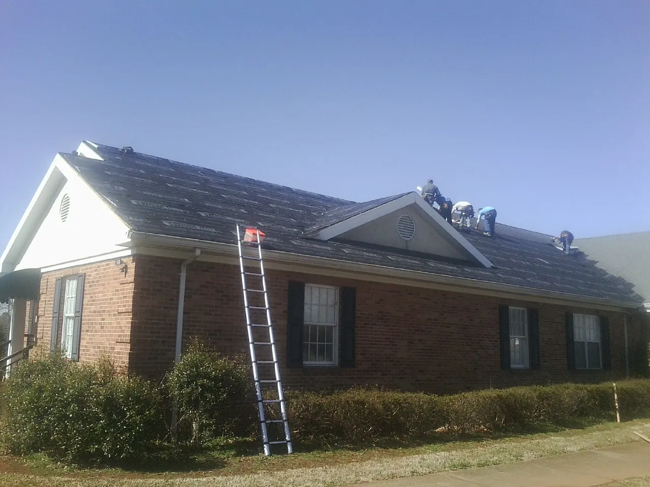 Crew tearing shingles off a brick ranch roof with a ladder set — Emergency Roof Repair work by our crew in Warsaw